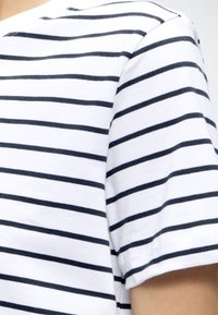 White fabric with evenly spaced, horizontal navy blue stripes on a short-sleeve garment, shown on a person’s shoulder and upper arm.