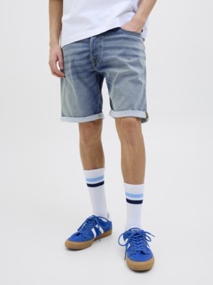 Shorts en denim bleu clair avec des ourlets retroussés, associés à des baskets bleues et des chaussettes blanches avec des rayures bleues. Design simple et décontracté.