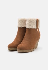 Botas de tornozelo em camurça castanha com um punho de pelo sintético creme. Sola texturizada leve com padrão de aderência e um botão decorativo de lado.