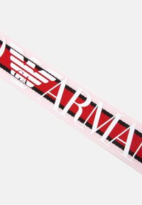 Ruban rayé rouge et noir avec un texte blanc en gras « ARMANI » et un logo. Le matériau semble tissé, avec une texture lisse.