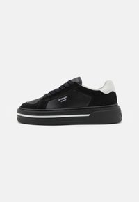 Svarte sneakers laget av lær og semsket skinn, med et elegant design, tykk såle og hvite detaljer på hælen. Merkevaren er synlig.