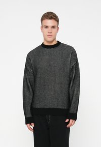 Maglione nero a maglia con una texture a coste, dotato di scollatura a girocollo, maniche lunghe e dettagli bianchi sottili in una fantasia verticale.
