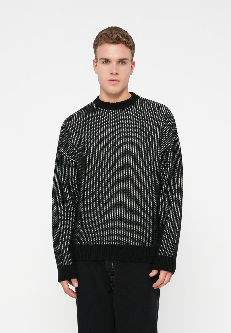 Maglione nero a maglia con una texture a coste, dotato di scollatura a girocollo, maniche lunghe e dettagli bianchi sottili in una fantasia verticale.