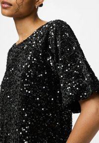 Melnas sekmju blūze ar teksturētu virsmu, īsām pūkainām piedurknēm un brīvu piegriezumu, ar apaļu kakla izgriezumu un spožiem sudrabainiem sekmjiem.