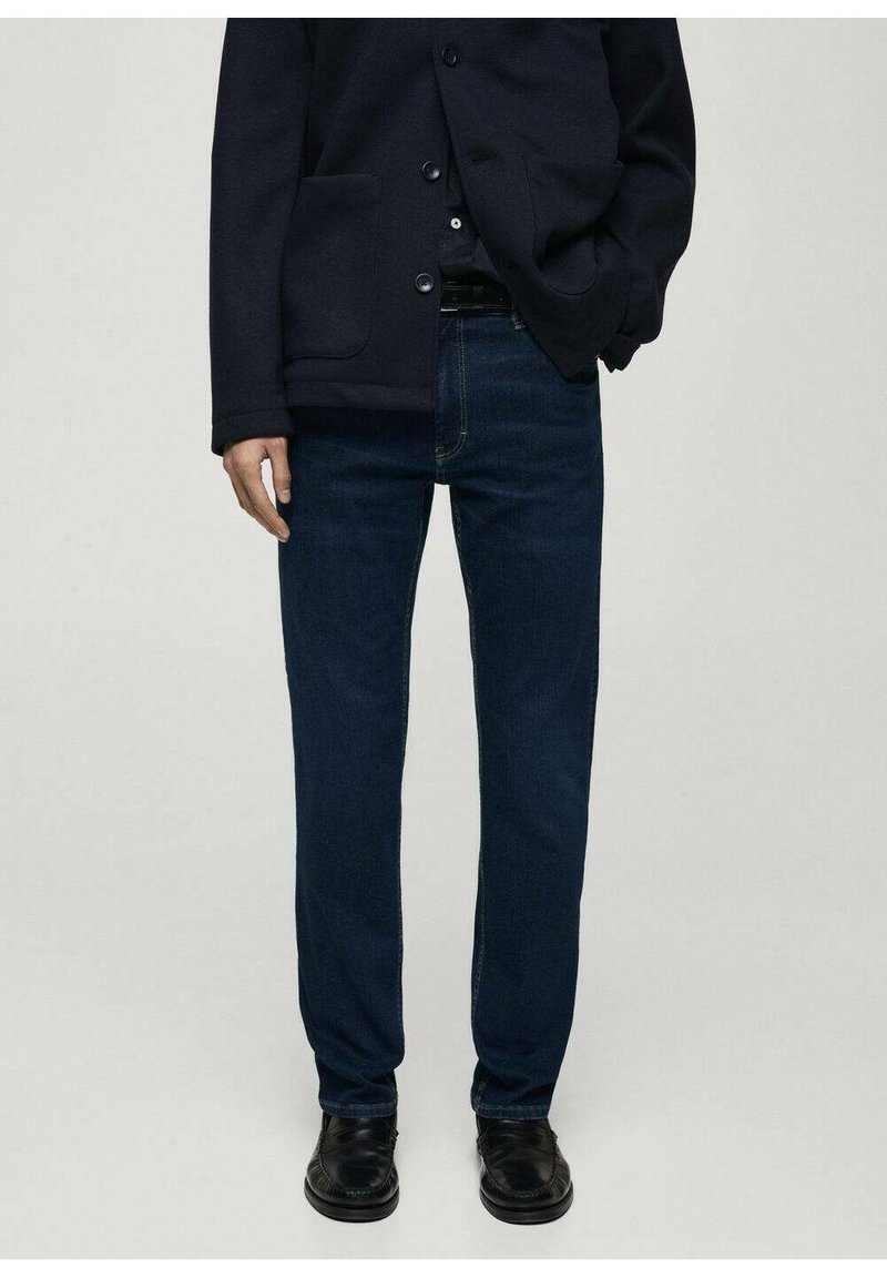 Tamno plave traperice od denima, ravnog kroja s lagano izblijeđenim završnim obradama. Uparene s crnom, dugmad-up vanjskom odjećom. Crne cipele.