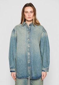Camicia di jeans in gradiente blu chiaro, con chiusura a bottoni frontale, colletto a punta e vestibilità oversize con maniche lunghe e orli a sbuffo.