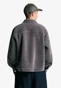 Szara kurtka ze sztruksu o luźnym kroju, z pionowymi prążkami, kołnierzem, mankietami na guziki oraz gładkim tyłem.