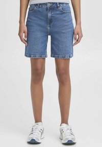 Shorts in denim di colore blu chiaro, lunghezza a metà coscia, con un classico design a cinque tasche e dettagli di cucitura visibili. Indossati con sneakers bianche.