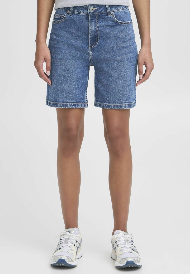 Shorts in denim di colore blu chiaro, lunghezza a metà coscia, con un classico design a cinque tasche e dettagli di cucitura visibili. Indossati con sneakers bianche.