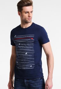 Navy blue cotton t-shirt featuring horizontal white and red stripes with ocean-themed graphics. Casual crew neck and short sleeves.