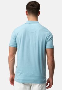 Lyseblå polo shirt med korte ærmer, flad krave og sideslidser; blød tekstur og enkelt design med en ensfarvet ryg.