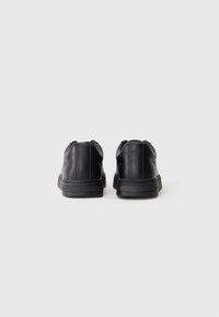 Sapatos de couro pretos com uma textura suave, perfil baixo, ponta arredondada e calcanhar almofadado. Sola de borracha com um discreto detalhe de costura.