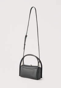 Μαύρη τσάντα χειρός από δέρμα με υφή, με στρογγυλεμένη επάνω λαβή, ρυθμιζόμενο μακρύ ιμάντα ώμου και κλείσιμο με χρυσή αγκράφα σε ουδέτερο φόντο.