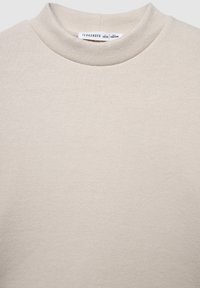 Beżowy sweter z półgolfem wykonany z miękkiego, teksturowanego materiału, z bezszwowym wzornictwem i minimalistyczną metką wewnątrz kołnierza.