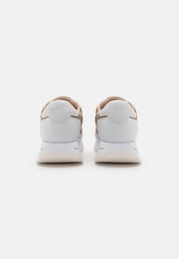 Baskets blanches avec un dos texturé marron, des accents en cuir lisse et une semelle légère. Présente le nom de la marque embossé sur le talon.