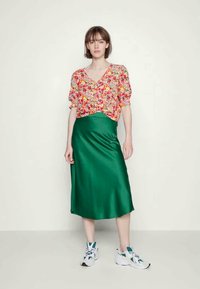 Blusa com padrão floral e mangas bufantes, combinada com uma saia midi de seda verde e ténis brancos com detalhes em azul.