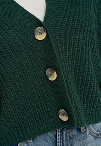 Cardigan lavorato a maglia verde scuro con scollo a V, texture a coste e tre bottoni rotondi color ambra sul davanti.
