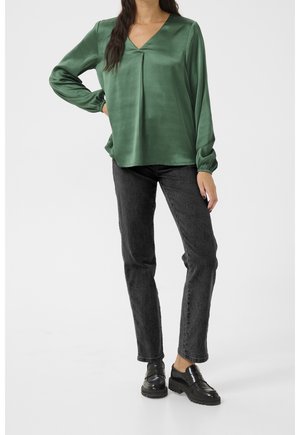 Grøn satinbluse med V-hals, lange ærmer og rynkede manchetter, kombineret med sorte denimjeans og sorte plateau loafers.