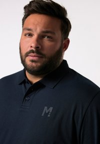 Mörkblå polo t-shirt i slätt tyg, med en treknapps knäppning och en subtil bröstlogga i en något ljusare nyans.