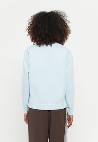 Felpa di colore blu chiaro con una vestibilità comoda, colletto e polsini a coste, e una texture liscia. Indossata con pantaloni scuri con bande laterali.