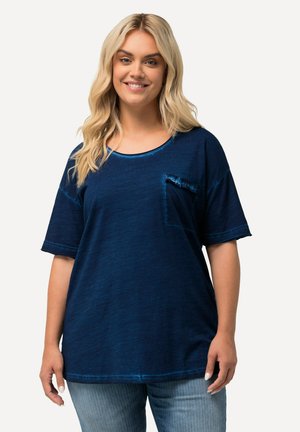 Námořnická modrá oversized tričko vyrobené z měkkého materiálu, s kulatým výstřihem, krátkými rukávy a malou přední kapsou s volánovým okrajem.