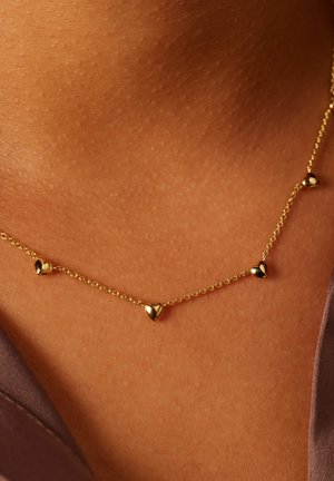 Gold chain necklace with five heart-shaped charms evenly spaced. Smooth texture, delicate design, worn against skin.