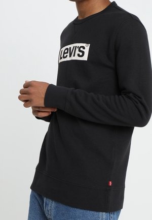 Sweatshirt noir avec un col rond, arborant un logo "Levi's" blanc bien visible sur le devant et des poignets et un ourlet côtelés. Design minimaliste.