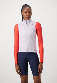 Chaleco ligero para ciclismo en lavanda pálido con mangas rojas brillantes. Cuenta con un alto cuello y cremallera frontal completa. Combinado con pantalones cortos de color azul oscuro.