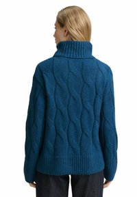 Pull en tricot turquoise avec un col montant, présentant un motif texturé en torsades et des bords côtelés aux hanches et aux poignets, fabriqué en fil épais.