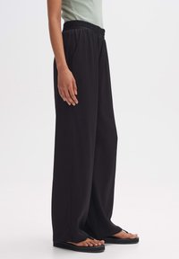 Svarta vida byxor med smockad midja, tillverkade av ett mjukt tyg. Silhuetten ger en lös passform, till par med platta sandaler.