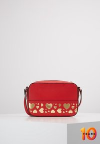 Borsa crossbody rossa con una texture liscia, caratterizzata da un motivo a cuore dorato intagliato lungo il fondo. Include una tracolla singola regolabile.