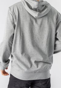 Felpa grigia con una texture morbida, dotata di cappuccio con coulisse e maniche lunghe. Il retro presenta un design semplice senza grafica visibile.