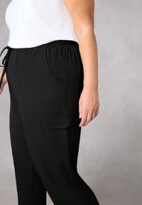 Svarta byxor med avslappnad passform, elastisk midja och dragsko, med sidofickor och en cargoficka, tillverkade av texturerat tyg.