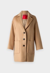 Abrigo de lana beige con cuello de pico, tres botones grandes y dos bolsillos frontales. Presenta una textura suave y un corte holgado.