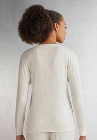 Světle šedý žebrovaný dlouhý rukáv s volným střihem. Má kulatý výstřih a kontrastní strukturované rukávy. Měkká tkanina, minimální švy.