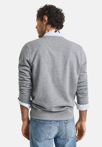 Grijze sweatshirt met lange mouwen, geribbelde manchetten en onderkant. Gepaard met een lichtblauw overhemd met kraag eronder, zichtbaar bij de manchetten.
