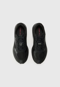 Zwarte sportieve schoenen met mesh en synthetische overlays, ronde neus, platte veters en een merk inlegzool met rode tekst.