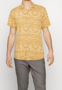 Camisa de manga corta, con botones, de color amarillo claro con un patrón similar a guijarros. El tejido parece ligero y tiene una textura suave.