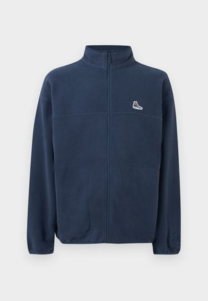 Navy blue full-zip fleece jacket with high collar, two front pockets, small white sneaker logo on left chest, and subtle embossed logo on left sleeve.