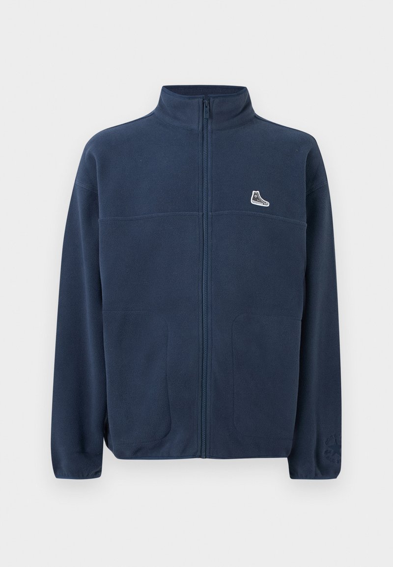 Navy blue full-zip fleece jacket with high collar, two front pockets, small white sneaker logo on left chest, and subtle embossed logo on left sleeve.