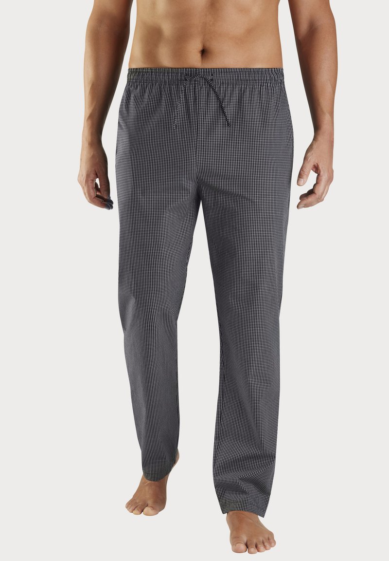 Vyriška torsas ir kojos, vilkintys juodai baltas kvadratinio rašto pižamines kelnes su raišteliu, stovintys basi ant vienodai paviršiaus.