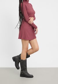 Körsbärsröd långärmad klänning med ribbat mönster, i kombination med knähöga svarta läderstövlar med silverdetaljer och spännen.