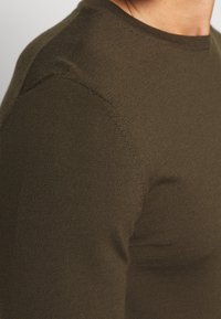 Olivgrüner Strickpullover mit Rundhalsausschnitt, taillierter Passform, gerippter Textur und glatten Nähten an den Schultern.