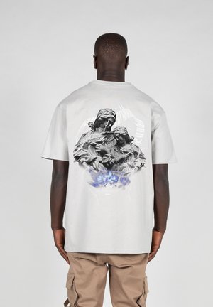 Lys grå bomull t-skjorte med et svart og hvitt grafisk trykk på baksiden, som viser to figurer innen et sirkulært design med blå detaljer.