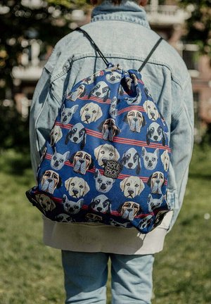Trekzak met koord, voorzien van blauwe stof met herhalende honden gezicht illustraties en rode strepen; zachte textuur en verstelbare schouderbanden.