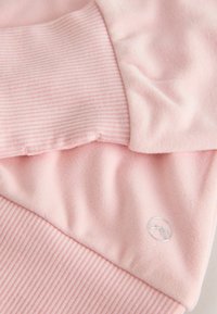 Šviesiai rožinė džemperis, pasižymintis lygia, minkšta tekstūra ir kontrastingu dryžuotu apvadu. Papuoštas skaidriu logotipu.