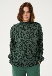 Top verde con un motivo astratto nero, dotato di collo alto e maniche lunghe. Realizzato in un tessuto testurizzato con una vestibilità rilassata.