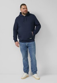 Felpa con cappuccio blu navy con motivo a trama, cappuccio regolabile con coulisse, tasca frontale, abbinata a jeans azzurri e scarpe da ginnastica bianche.