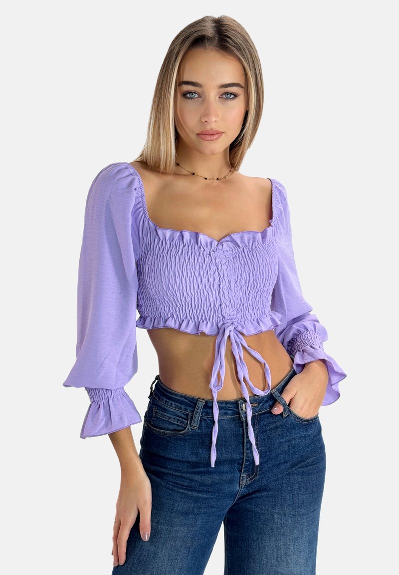 Lilla cropped top med smocket tekstur, firkantet halsudskæring og puffede ærmer. Har en bindedetail i taljen. Parret med mørk denim jeans.