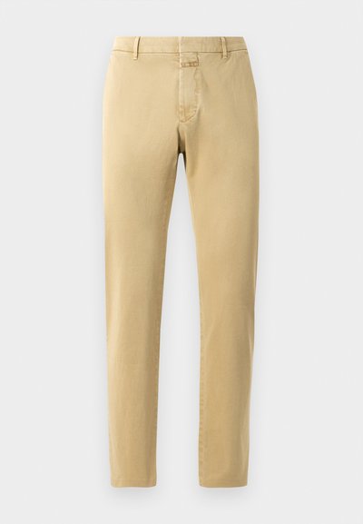 Chino beige avec une coupe ajustée et un tissu en coton lisse. Comprend une fermeture éclair, des passants de ceinture et des détails de couture minimalistes.
